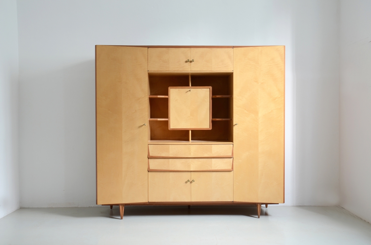 Mobile contenitore in acero biondo con edicola centrale a giorno e anta a ribalta che nasconde un piccolo scrigno con ripiani inclinati e cassetto. Due grandi cassetti e ante con ripiani, piedi fuori asse. Manifattura Italiana 1960ca.
