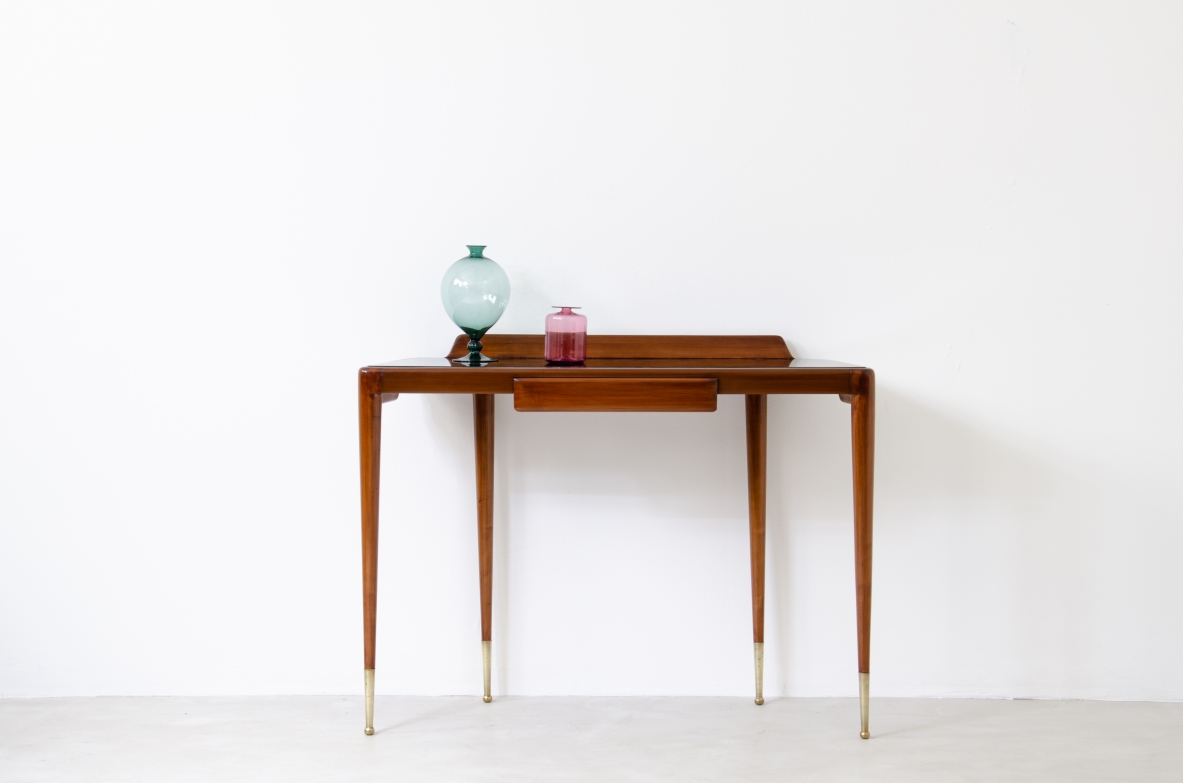 Elegante console con sottili gambe in noce biondo e lunghi puntali in ottone. Cassetto centrale e piano in vetro opaline nero.  Manifattura Italiana 1950ca.