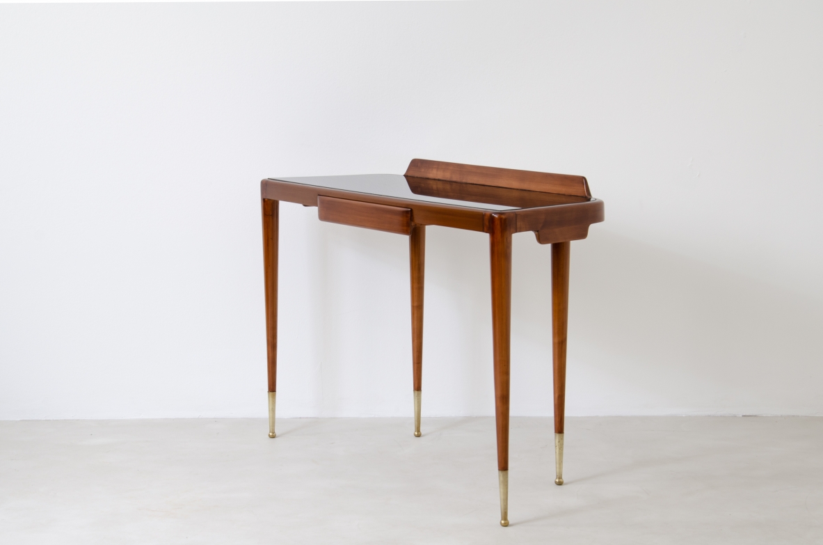 Elegante console con sottili gambe in noce biondo e lunghi puntali in ottone. Cassetto centrale e piano in vetro opaline nero.  Manifattura Italiana 1950ca.