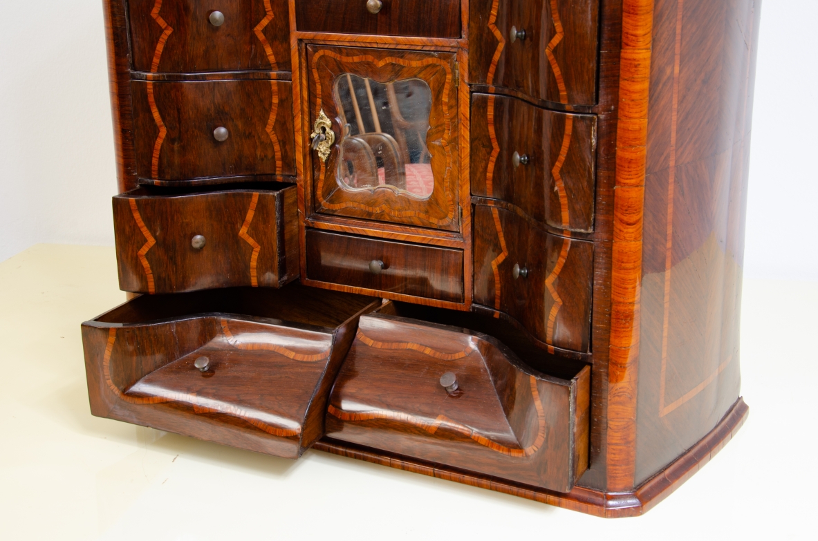 Genoese cabinetry, c. 1750, coin cabinet in violet wood threaded in rose wood with wavy front, central aedicule with shaped door and central mirror.