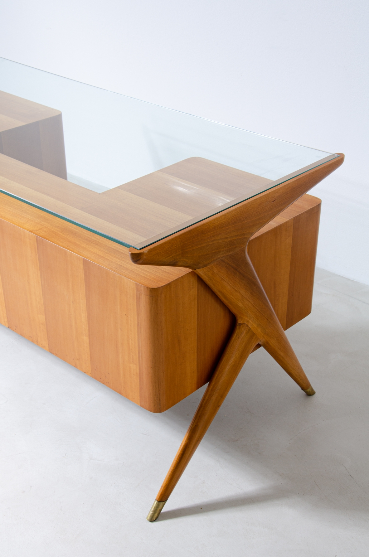 Writing table in blond wood with thick glass top and sculptural side uprights with brass tips.  1950's Italian manufacture.