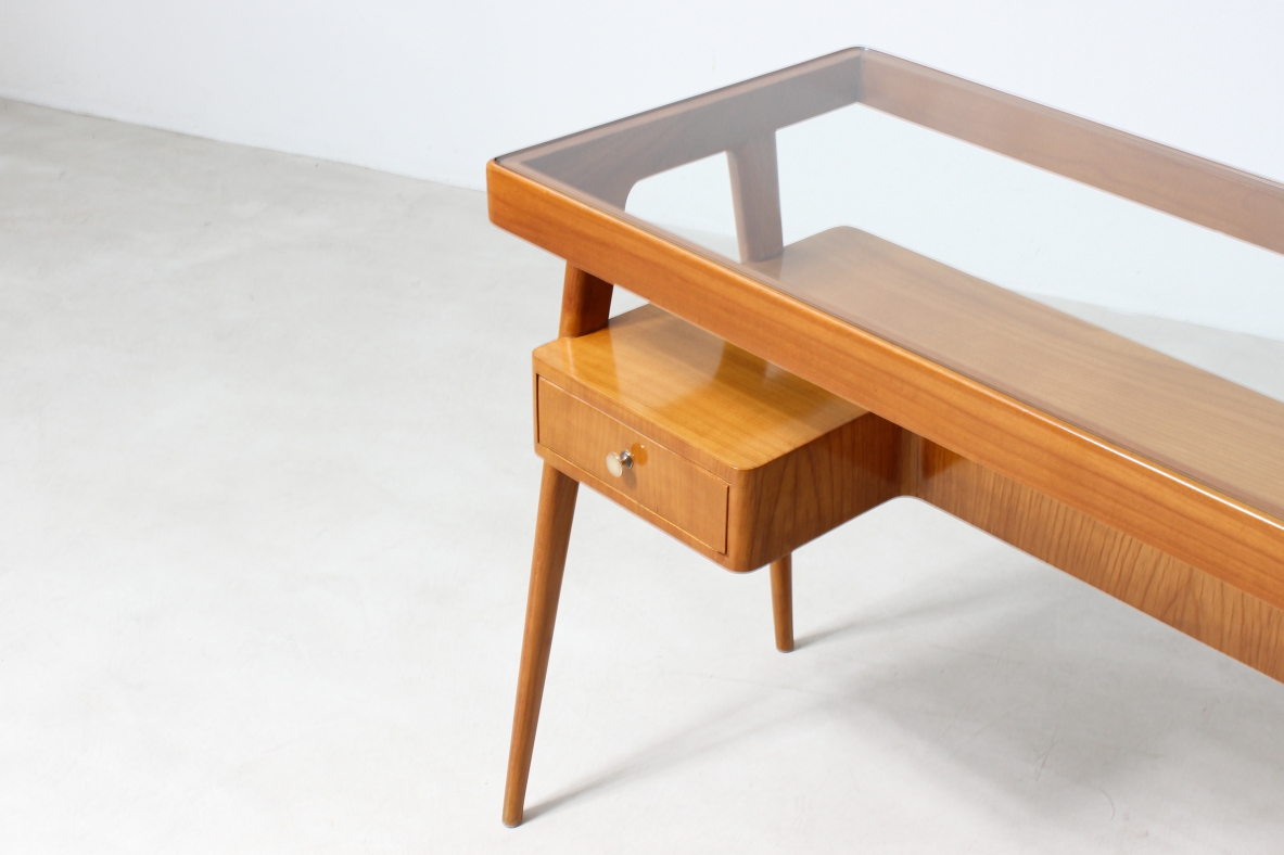 Piccolo scrittoio in legno biondo con piano in vetro e ripiano sagomato con due cassetti sul fronte.
