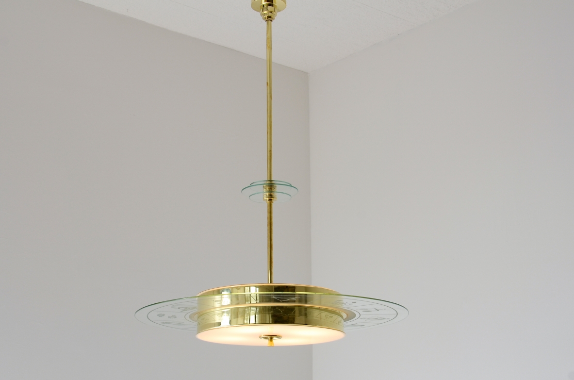 Grande lampadario in ottone con vetro molato e decorato con i disegni dello zodiaco e due vetri bianco lattimo. Stelo in ottone con tre dischi in vetro trasparente molato.  Manifattura Brusotti Milano, 1930-40ca.