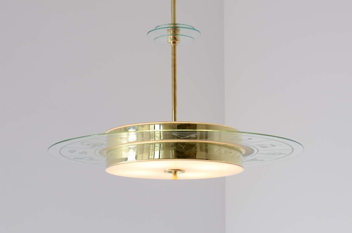 Grande lampadario in ottone con vetro molato e decorato con i disegni dello zodiaco e due vetri bianco lattimo. Stelo in ottone con tre dischi in vetro trasparente molato.  Manifattura Brusotti Milano, 1930-40ca.
