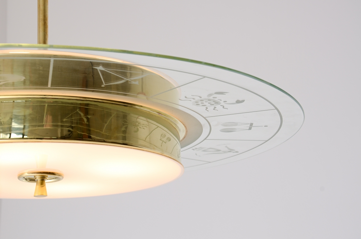 Grande lampadario in ottone con vetro molato e decorato con i disegni dello zodiaco e due vetri bianco lattimo. Stelo in ottone con tre dischi in vetro trasparente molato.  Manifattura Brusotti Milano, 1930-40ca.