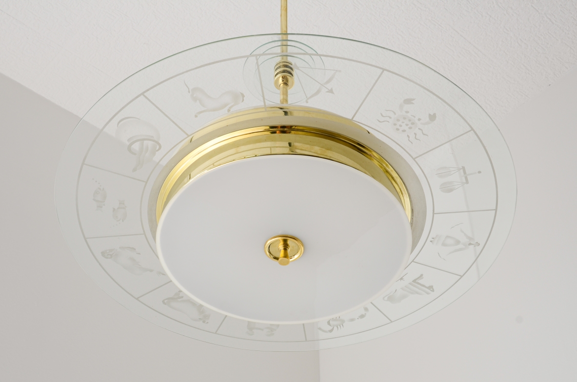 Grande lampadario in ottone con vetro molato e decorato con i disegni dello zodiaco e due vetri bianco lattimo. Stelo in ottone con tre dischi in vetro trasparente molato.  Manifattura Brusotti Milano, 1930-40ca.