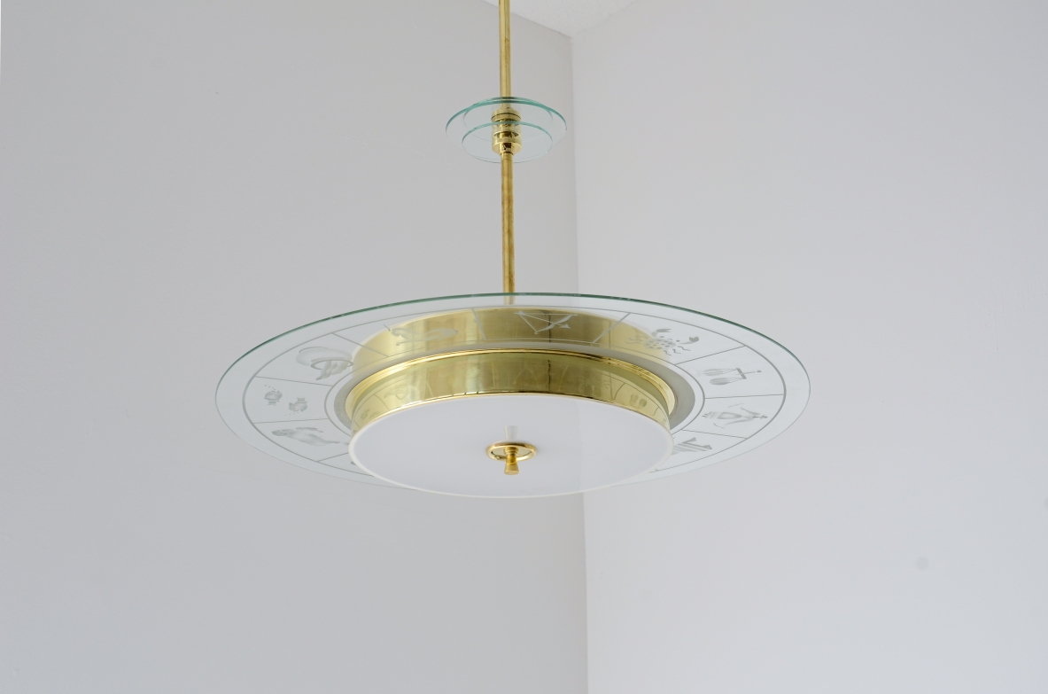 Grande lampadario in ottone con vetro molato e decorato con i disegni dello zodiaco e due vetri bianco lattimo. Stelo in ottone con tre dischi in vetro trasparente molato.  Manifattura Brusotti Milano, 1930-40ca.