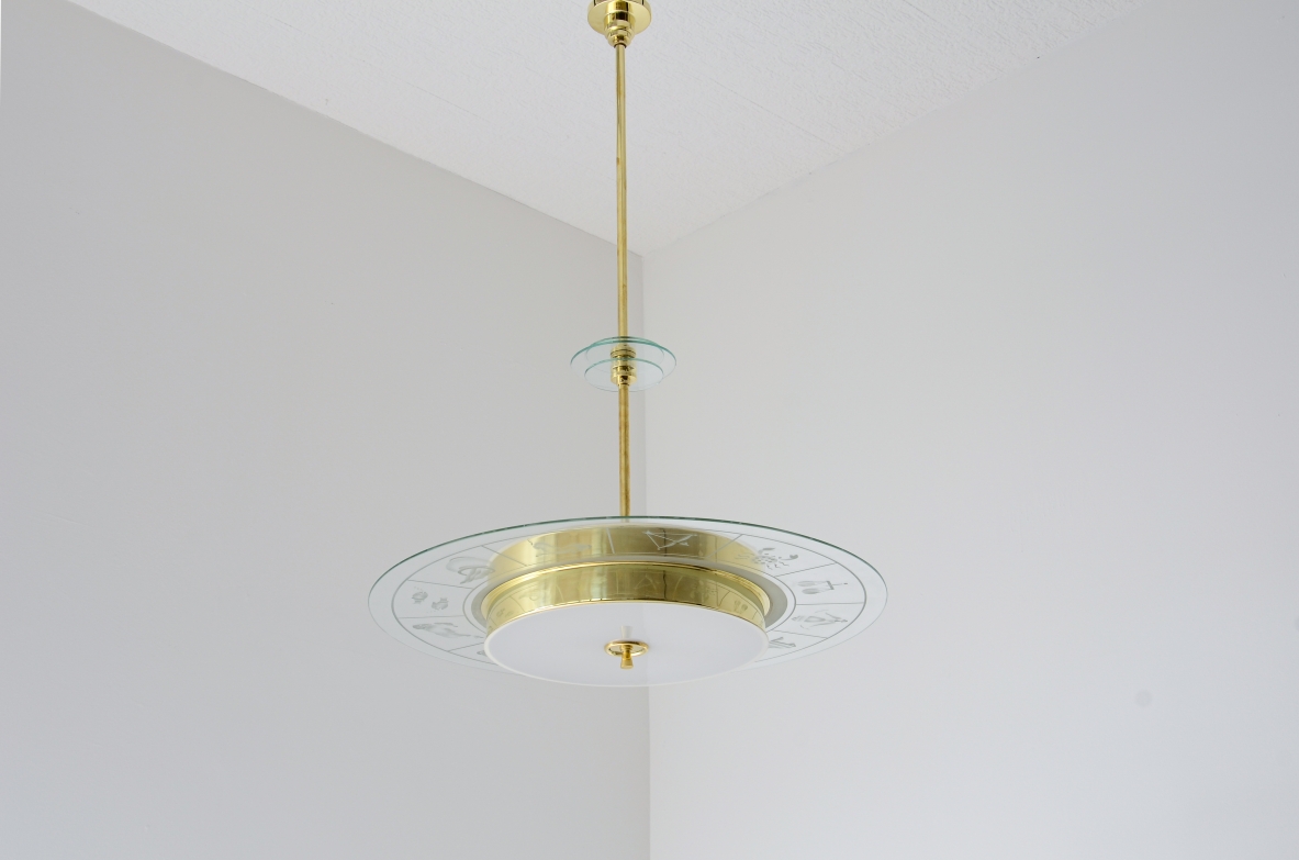 Grande lampadario in ottone con vetro molato e decorato con i disegni dello zodiaco e due vetri bianco lattimo. Stelo in ottone con tre dischi in vetro trasparente molato.  Manifattura Brusotti Milano, 1930-40ca.