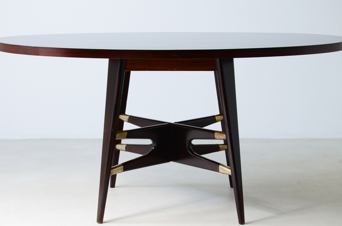 Gianni Vigorelli   Elegante tavolo ovale in legno tinto con montanti a quattro gambe e importante crociera con puntali in ottone.  Manifattura italiana, attr. Vigorelli. 1950ca.