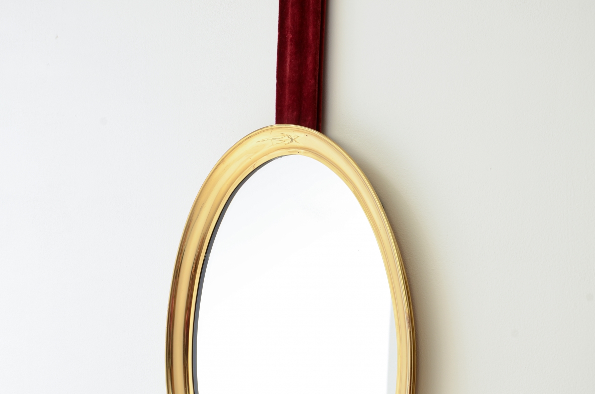 Mirror in shaped brass hanging from an original velvet ribbon and fixed to the wall using a brass disc.  Italian manufacture, 1950s/60s.