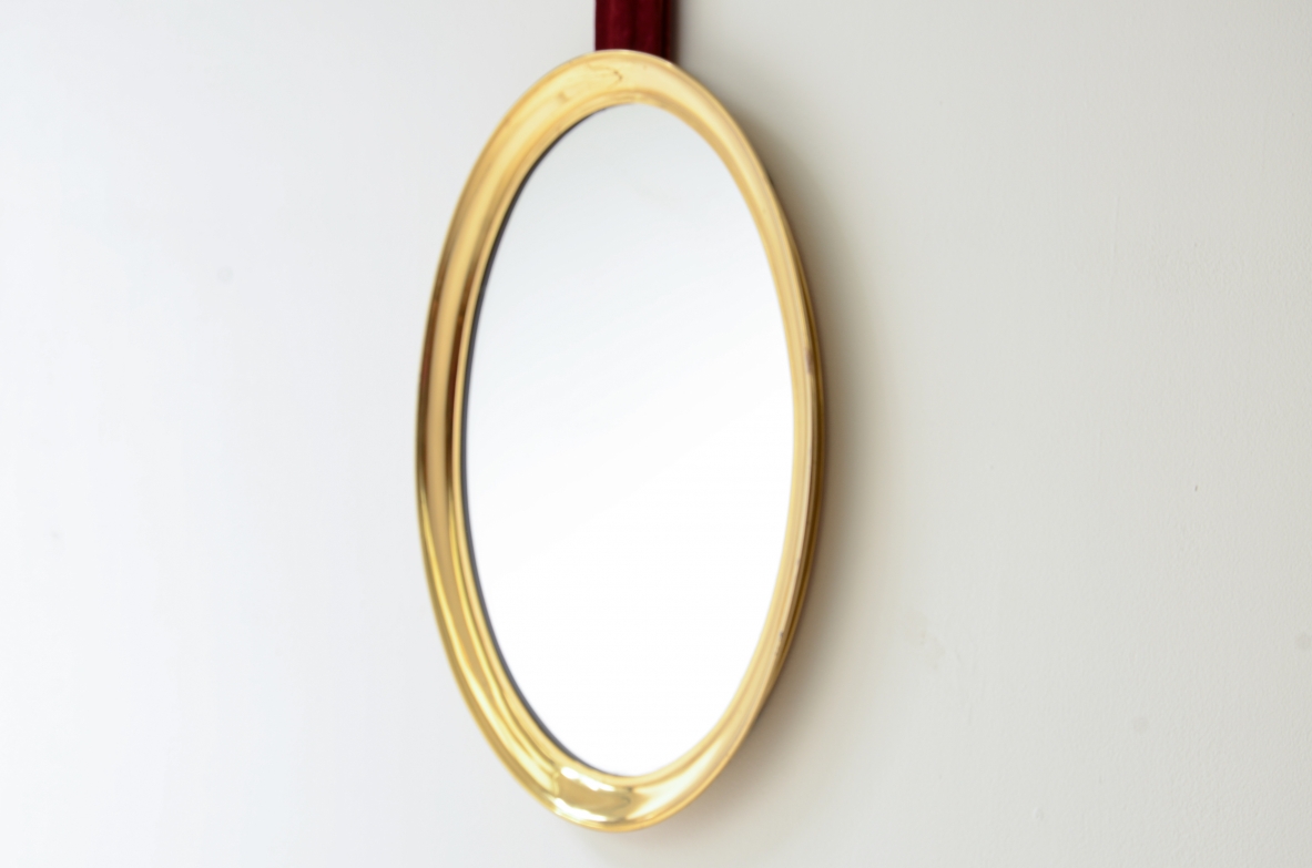 Mirror in shaped brass hanging from an original velvet ribbon and fixed to the wall using a brass disc.  Italian manufacture, 1950s/60s.