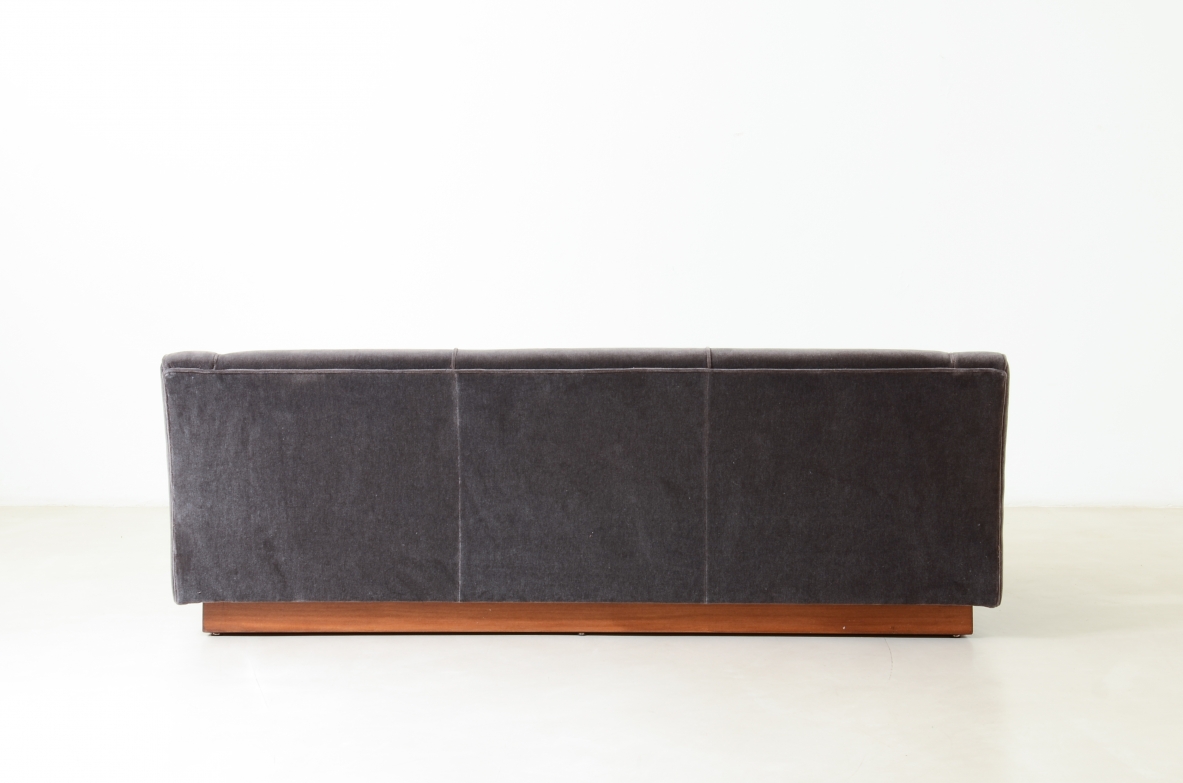 Three-seater sofa with wooden base and padded velvet upholstery.