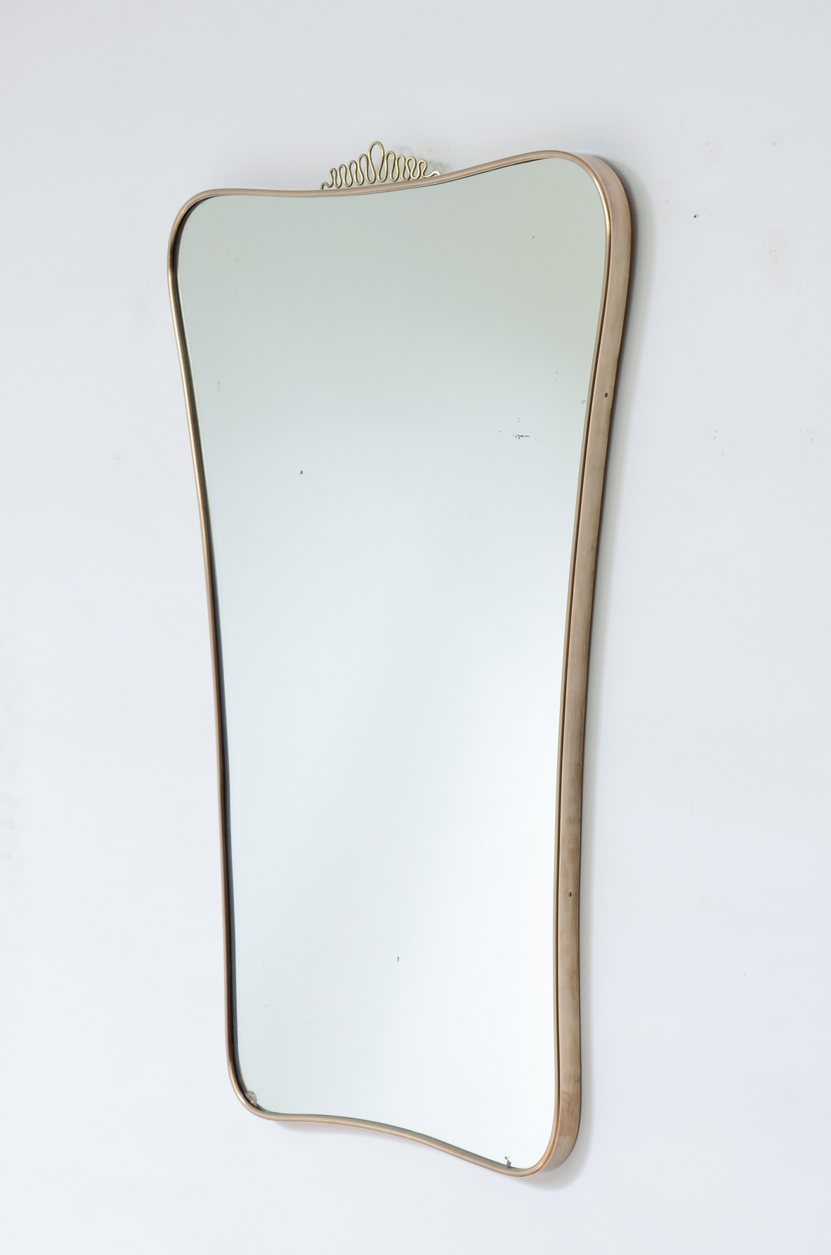 Elegante specchiera con cornice sagomata in ottone. Attribuibile a Gio Ponti. Manifattura italiana, anni ’50.