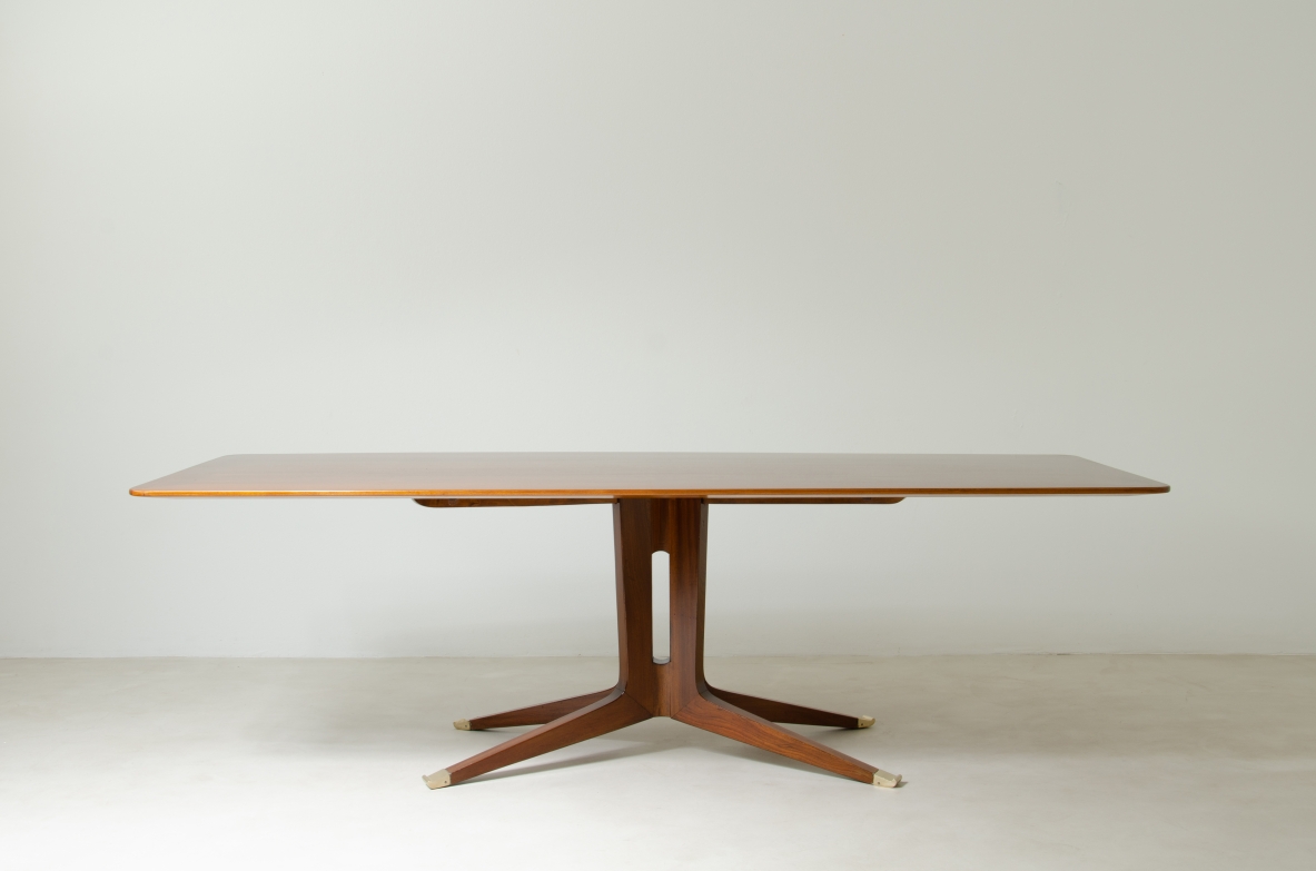 Grande tavolo in mogano con piano sagomato e gamba con fusto centrale e quattro razze con elegante puntale in ottone.  Manifattura italiana 1950ca.