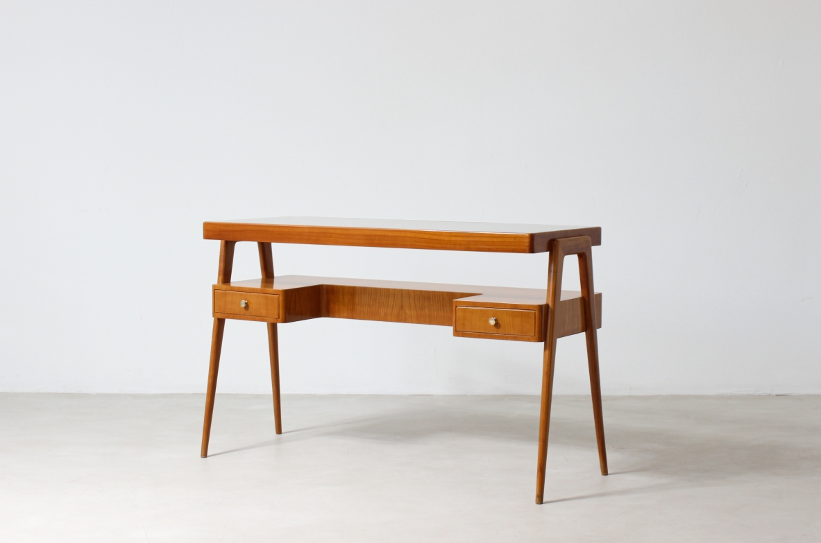 Small desk in blond wood with glass top and shaped shelf with two drawers on the front.