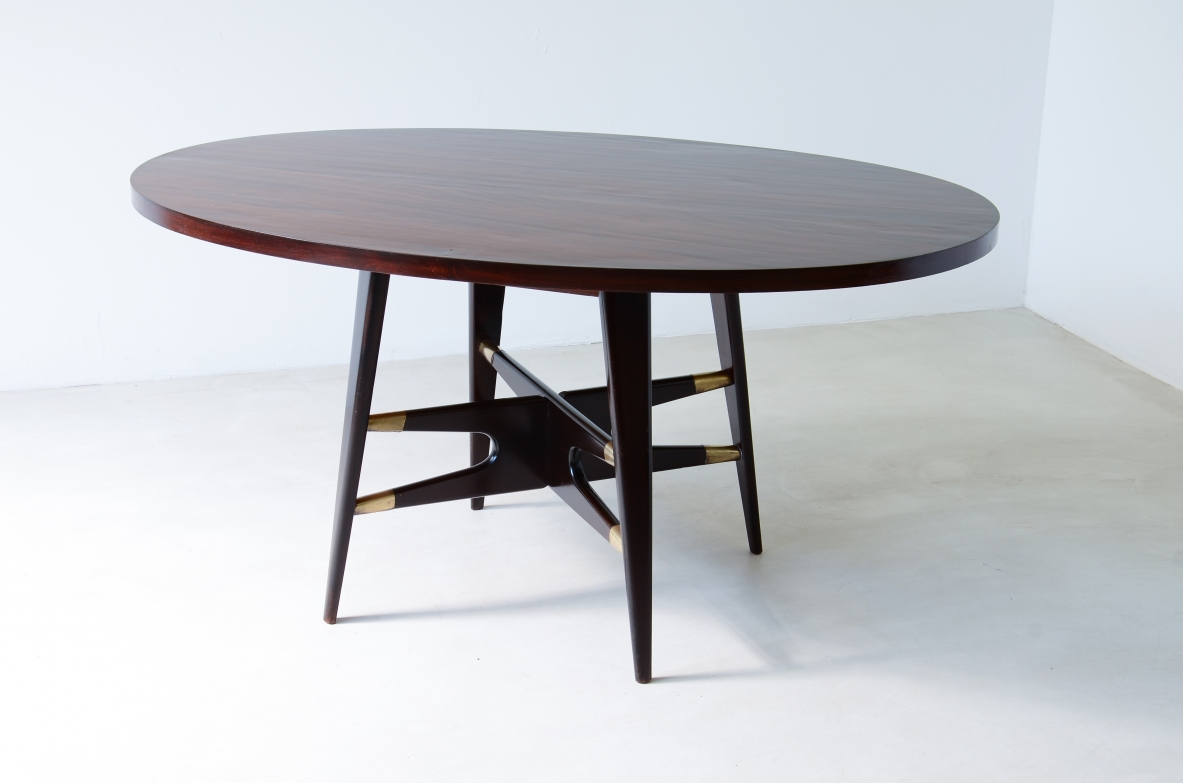 Gianni Vigorelli   Elegante tavolo ovale in legno tinto con montanti a quattro gambe e importante crociera con puntali in ottone.  Manifattura italiana, attr. Vigorelli. 1950ca.